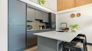 A modern kitchen with grey cabinets, a white countertop, and a brick wall. There are two potted plants on the counter. - Stay Angels Blonk Street Apartments (Sheffield)