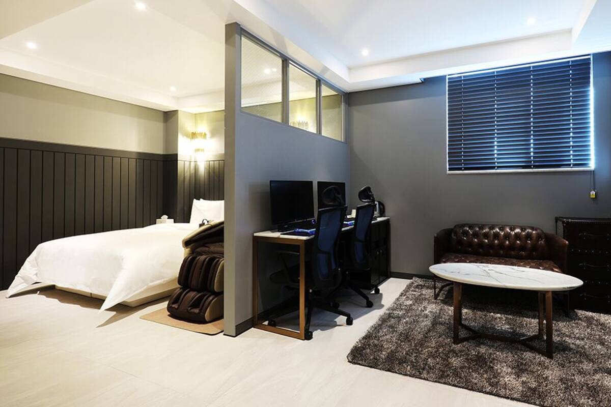 A modern hotel room with a bed, desk, chair, and a small round table.