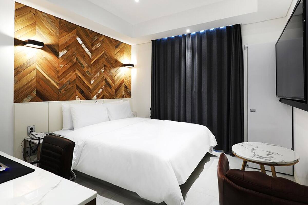 A hotel room with a large bed, a desk with a computer, a small round table, and a TV mounted on the wall.