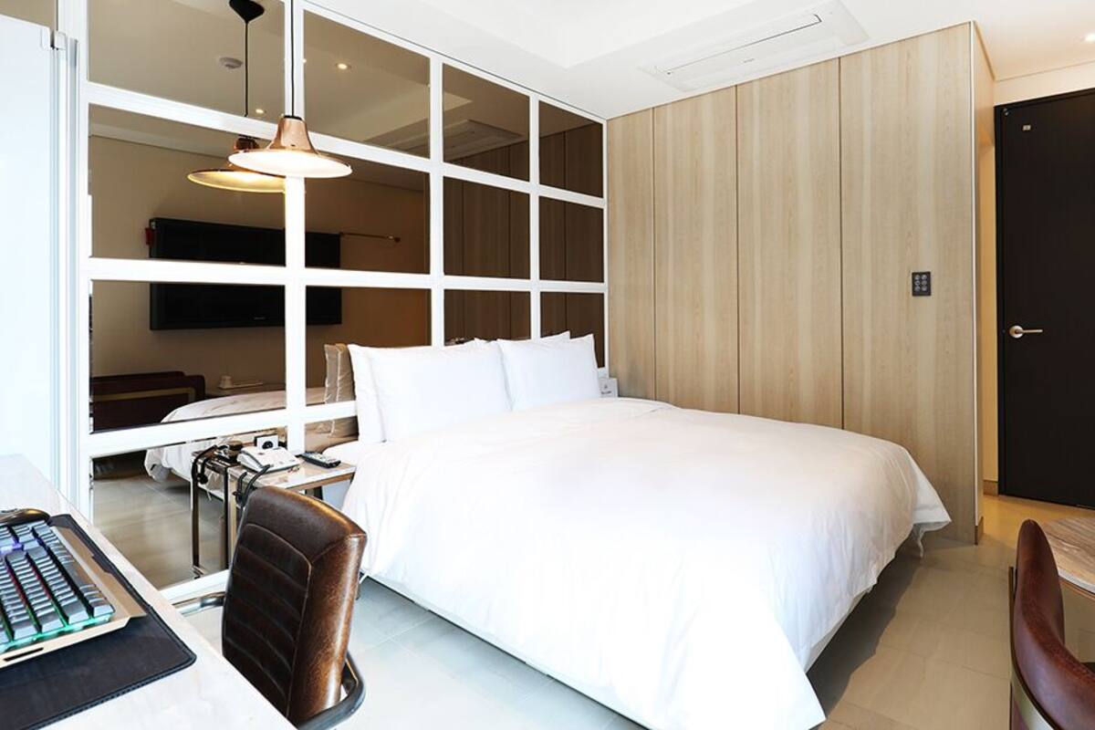 A modern hotel room with a large bed, a desk with a computer, a chair, and a TV mounted on the wall.
