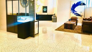 A lobby with a glass partition, a clock, a Starbucks sign, a trash bin, and a blue abstract painting. - Alma Business Hotel (Jincheon)