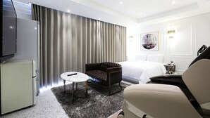 A modern hotel room with a bed, a leather armchair, a small round table, a television, and a minibar. - Alma Business Hotel (Jincheon)