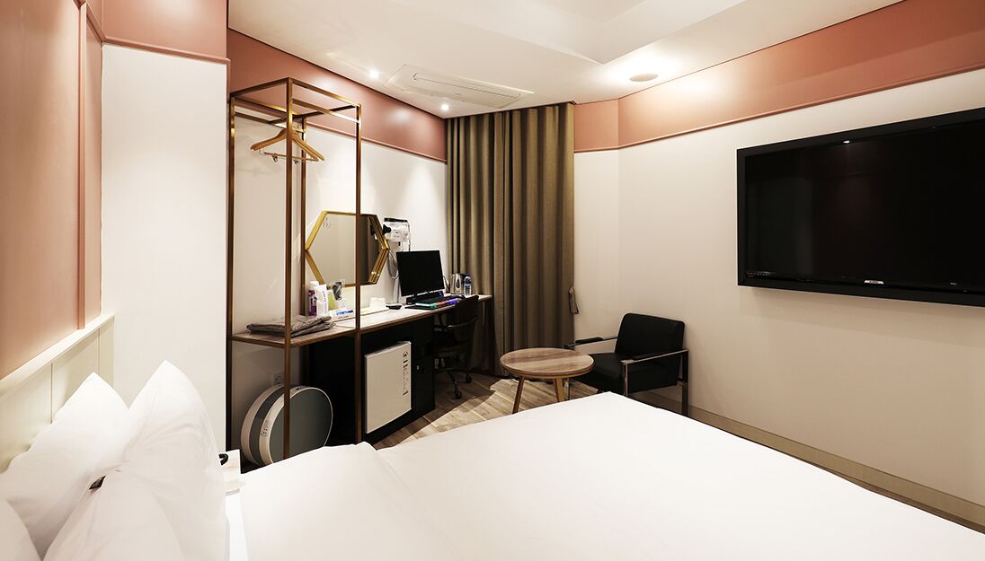 Habitación de hotel con cama, escritorio con ordenador, silla, televisor y armario.
