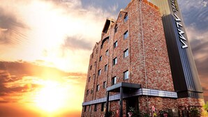 A modern hotel with a prominent vertical sign, multiple windows, and a brick facade. - Alma Business Hotel (Jincheon)