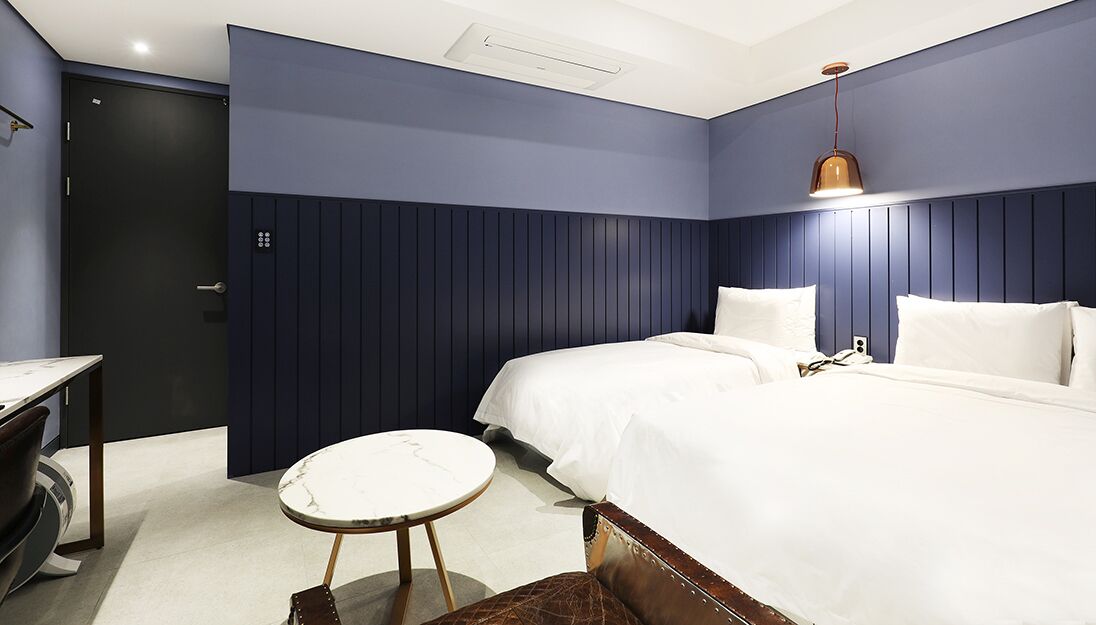 Una habitación de hotel moderna con una cama grande, una mesa redonda y una pared decorada en tono azul oscuro.