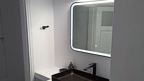 Ein modernes Badezimmer mit einem weißen Waschtisch, einem schwarzen Becken und einem Spiegel.