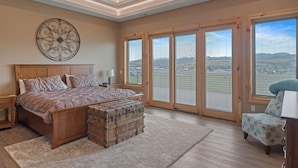 Een slaapkamer met een groot bed, een dressoir, een decoratief wandobject en grote schuifdeuren die uitkomen op een balkon.
