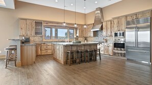 Een ruime keuken met houten kastjes, een groot eiland met krukken, roestvrijstalen apparatuur en een betegelde achterwand.