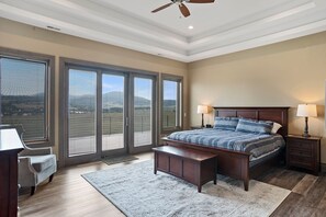 A bedroom with a large bed, two bedside tables with lamps, a wooden bench, a chair, and a view through large sliding doors. - Spacious w/ Amazing View, Large Deck Spacious Open Plan Near Spearfish (Spearfish)