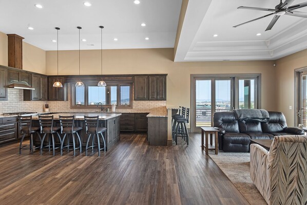 A modern kitchen with dark wood cabinets, a central island with bar stools, and a dining area with a leather sofa and patterned armchair. - Spacious w/ Amazing View, Large Deck Spacious Open Plan Near Spearfish (Spearfish)