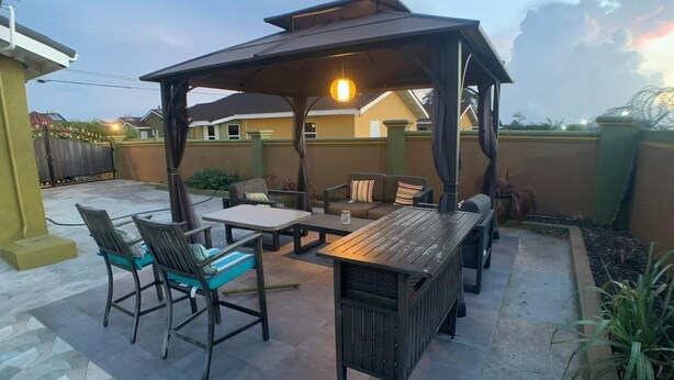 An outdoor patio with a wooden table and chairs, a covered seating area, and a hanging light fixture. - Luxurious Home (Draxhall)