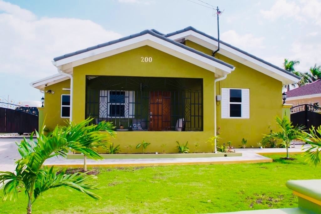 A yellow house with the number 200, a covered porch, and small palm trees in the yard.