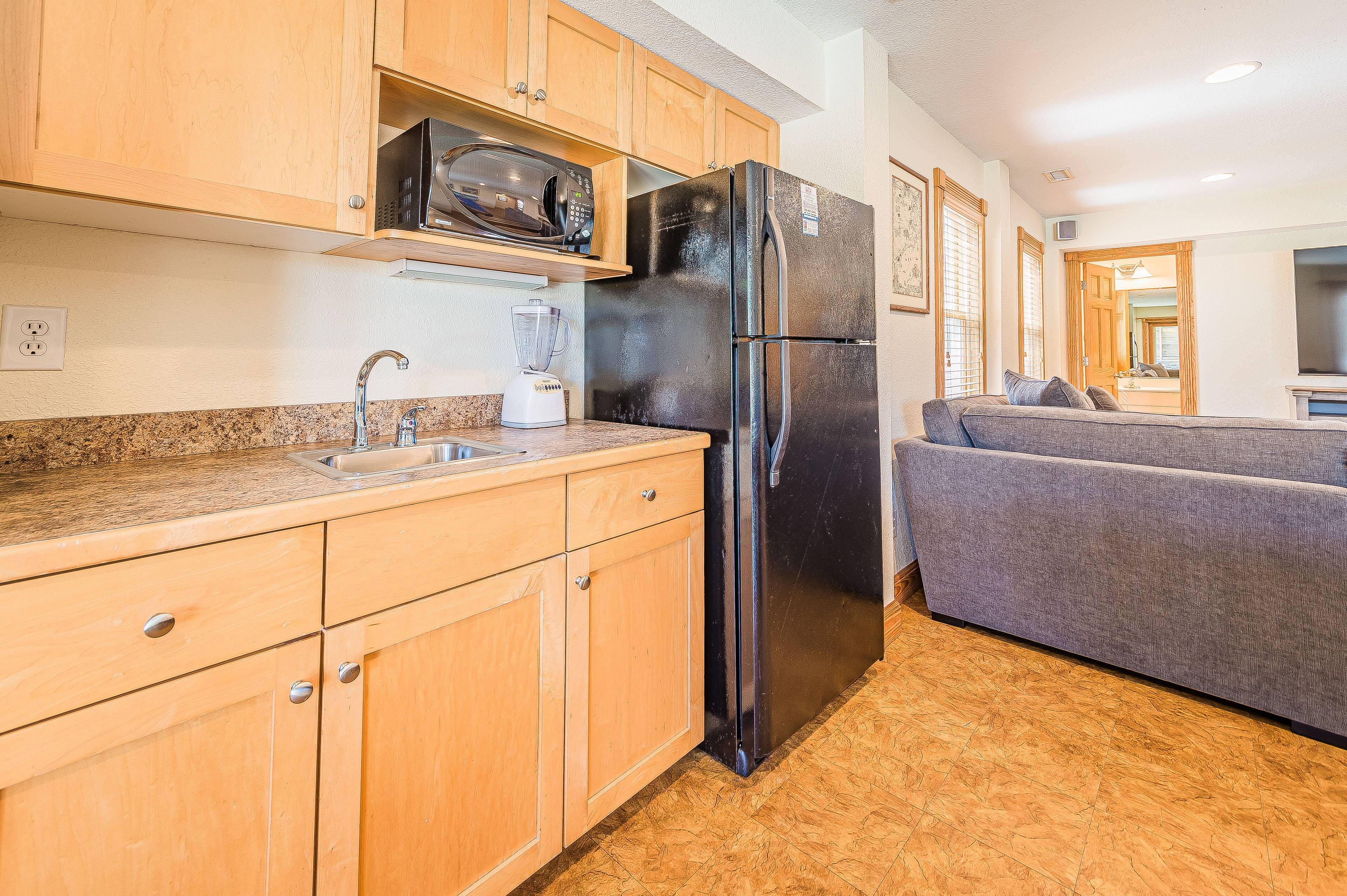 A compact kitchen with wooden cabinets, a black refrigerator, a microwave, and a built-in oven.