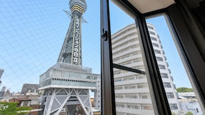 A view through a window of a building with a tall tower and a modern glass structure. - The Only View (Osaka)