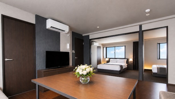 A modern hotel room with a flat-screen TV, a wooden table with a vase of flowers, a bed with two pillows, and a large window. - The Only View (Osaka)