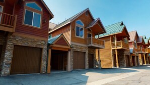 Une rangée de maisons modernes à plusieurs étages, dotées de façades en bois et d’éléments décoratifs en pierre, avec de grandes portes de garage et des balcons.