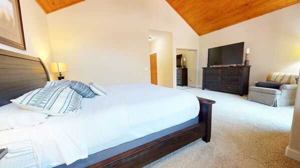 A bedroom with a large bed, a wooden ceiling, a TV, a dresser, and a sofa.