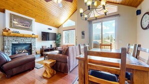 Un salon chaleureux avec une cheminée en pierre, des canapés en cuir, une table à manger en bois et une grande fenêtre offrant une vue sur les montagnes.