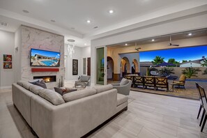 A modern living room with a fireplace, a television mounted on the wall, and a dining area with outdoor seating.