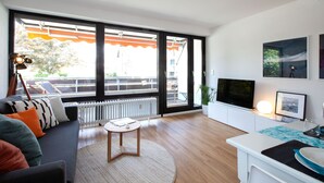 A modern living room with a sofa, a coffee table, a TV, and a dining area with a table and chairs. - Glücks-Quartier "Waldhufe 1" (Bad Liebenzell)