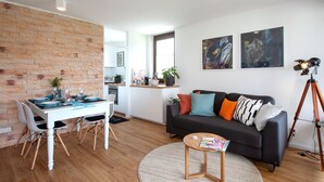 A modern living room with a dining area, a black sofa with colorful cushions, and a small wooden table. - Glücks-Quartier "Waldhufe 1" (Bad Liebenzell)