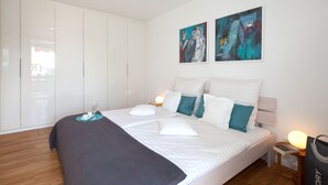 A modern bedroom with a large bed, white bedding, teal and white pillows, a bedside table with a lamp, and artwork on the wall. - Glücks-Quartier "Waldhufe 1" (Bad Liebenzell)