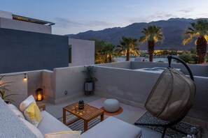 Une terrasse sur le toit, aménagée avec un canapé, une table et des chaises, d’où l’on peut admirer un paysage montagneux parsemé de palmiers.