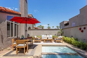 A pool area with a table and chairs, a red umbrella, and a view of palm trees. - Caballeros - Private Condo w/ Pool, Spa & Mountain Views (Palm Springs)