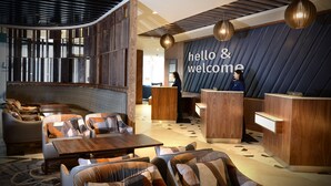 Un moderno vestíbulo de hotel con mostrador de recepción, zona de estar y un cartel que dice 'hello & welcome'.