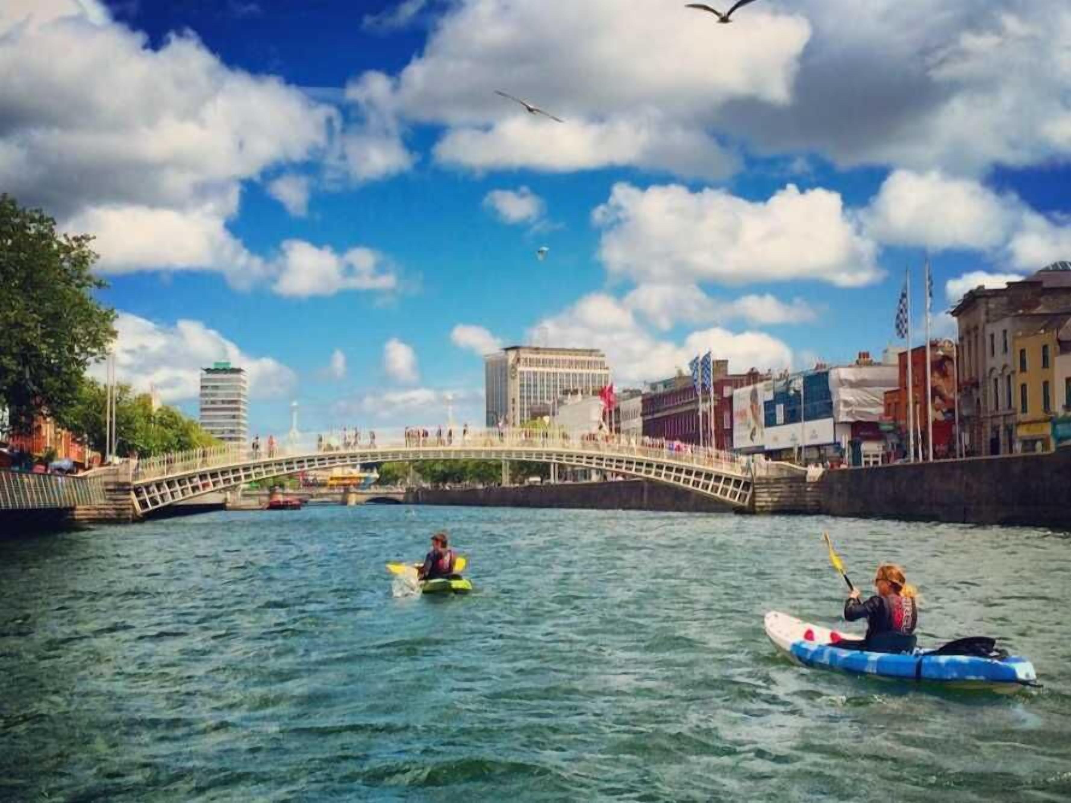 A river with kayakers, a bridge, and buildings in the background.