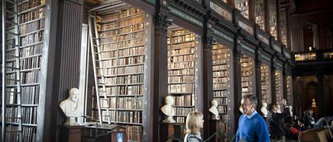 Interior de una biblioteca con altas estanterías, bustos de esculturas y una escalera central.
