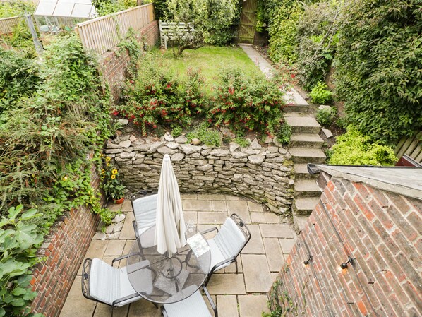 A patio with a table and chairs, surrounded by a stone wall and a brick wall with a wooden gate.