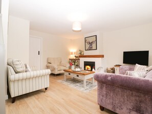 A living room with a fireplace, striped armchairs, a purple sofa, and a television. - Blueberry Cottage (Dorchester)
