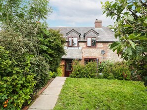 A traditional brick house with a sloped roof, a chimney, and a small front garden with a pathway leading to the entrance. - Blueberry Cottage (Dorchester)
