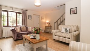 A living room with a sofa, armchair, coffee table, and a staircase. - Blueberry Cottage (Dorchester)
