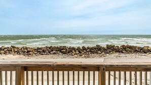 Een houten terras met uitzicht op een rotsachtige kustlijn, waar golven op het strand breken.