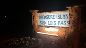 Een stenen bord met de tekst 'TREASURE ISLAND SAN LUIS PASS' verlicht bij nacht.