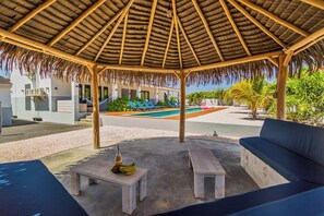 A covered outdoor seating area with a pool in the background.