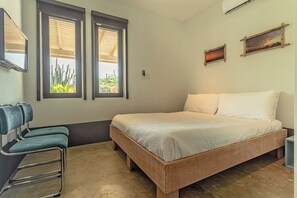 A bedroom with a bed, two windows, a chair, and a wall-mounted TV. - Ocean View Lounge: 5BR Villa w Private Pool Patio (Noord)