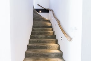 A staircase with a wooden handrail and a wall-mounted light fixture. - Ocean View Lounge: 5BR Villa w Private Pool Patio (Noord)