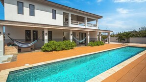 Una casa moderna de dos pisos con piscina, terraza de madera y hamaca.