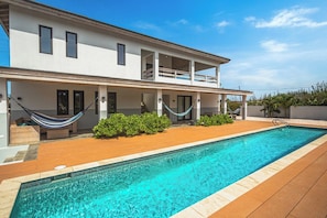 A modern two-story house with a swimming pool, wooden deck, and a hammock. - Ocean View Lounge: 5BR Villa w Private Pool Patio (Noord)