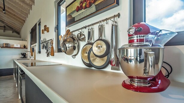 Una cocina con diseño moderno, que incluye una isla grande, ollas colgantes y una batidora KitchenAid roja.