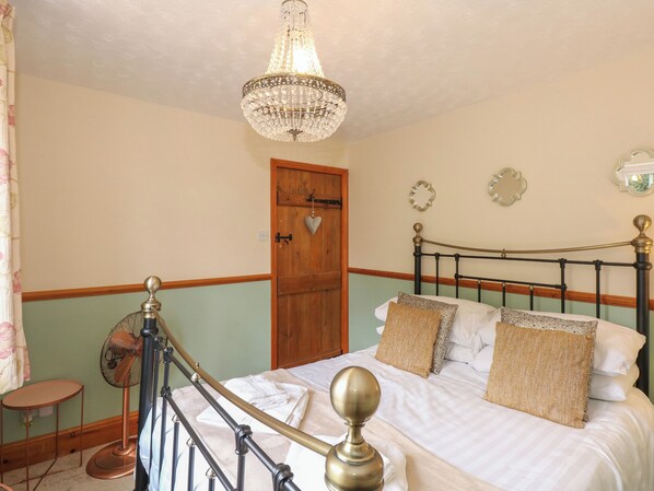 Une chambre à coucher avec un lit, une porte en bois, un ventilateur et un lustre.