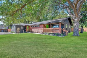 Una casa moderna con terraza de madera, un porche delantero y un gran árbol en el jardín.