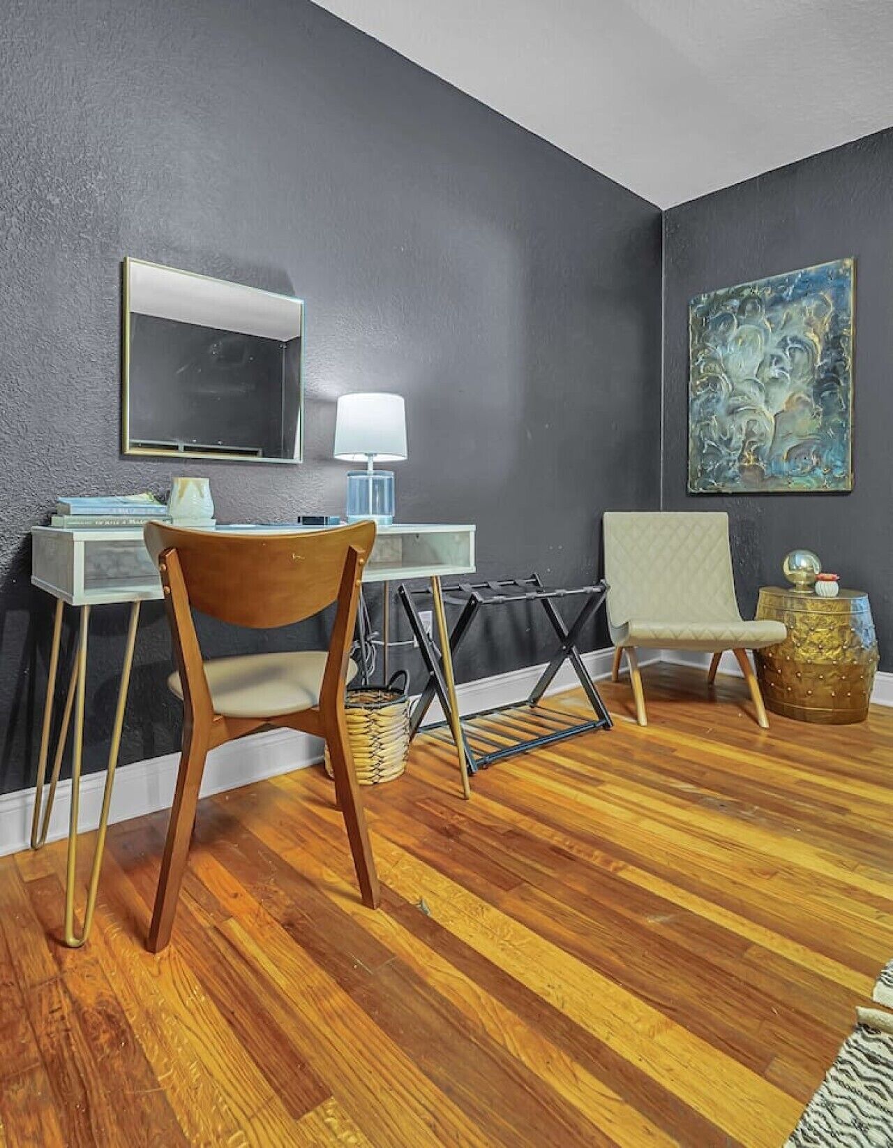 Une pièce comprenant un bureau, deux chaises, une lampe, un téléviseur et un tableau accroché au mur.