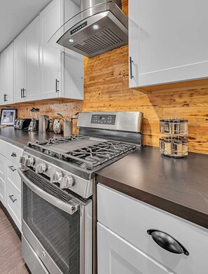 Eine moderne Küche mit Edelstahlgeräten, weißen Schränken und einer Wand in Holzoptik.