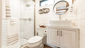 A bathroom with a glass shower enclosure, a toilet, a sink with a mirror, and a cabinet. - Deer Creek Tiny Container Home-12 Min to Magnolia (Waco)