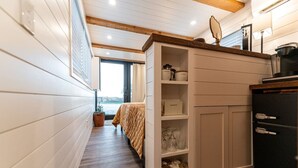 A narrow hallway with a bed, a white cabinet with shelves, and a black cabinet. - Deer Creek Tiny Container Home-12 Min to Magnolia (Waco)