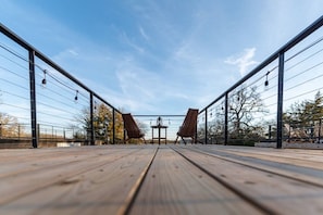 A wooden deck with two wooden chairs and a table, surrounded by metal railings and trees. - Cozy Tiny Container Home-The Outwest (Waco)